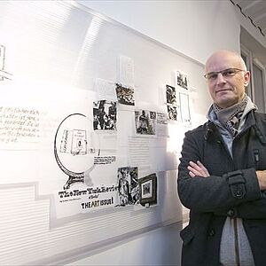 Bernhard Gwiggner steht neben seinem an der Wand aufgehängten Werk: mit Lackstift auf Transparentpapier gezeichnete USA-Eindrücke