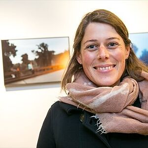 Die Künstlern Annelies Senfter im Halbportrait, im Hintergrund sind drei ihrer Bilder zu sehen.