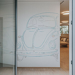 Blick durch eine geöffnete Glatür auf einen VW Käfer an der gegenüberliegenden Wand