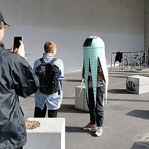 Person mit über dem Oberkörper gestülpten Kunstobjekt; die Form ähnelt einer Krake