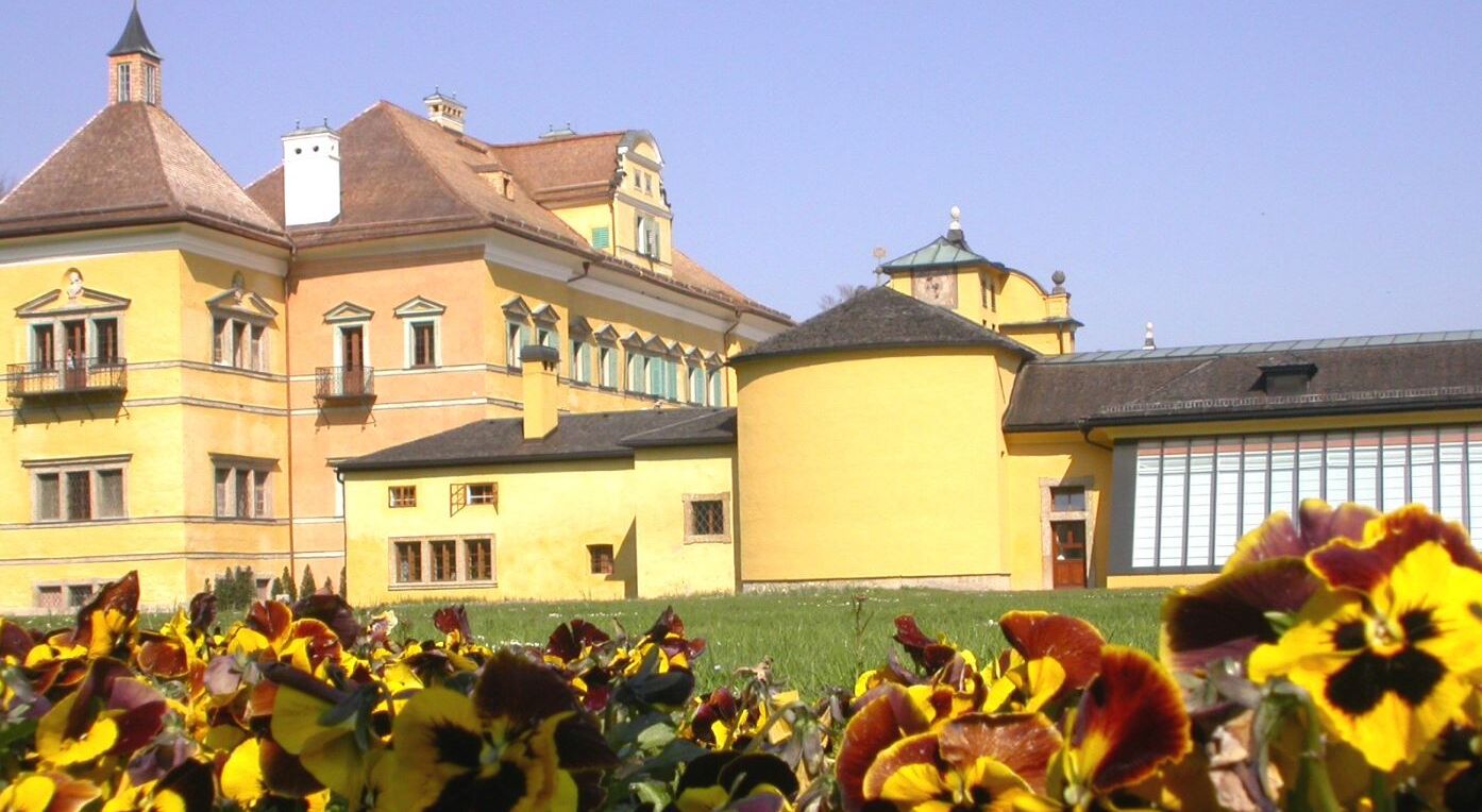 Schloss Hellbrunn mit Blumenbeeten Das Schloss Hellbrunn, fotografiert von außen, vor schönen Blumenbeeten.
