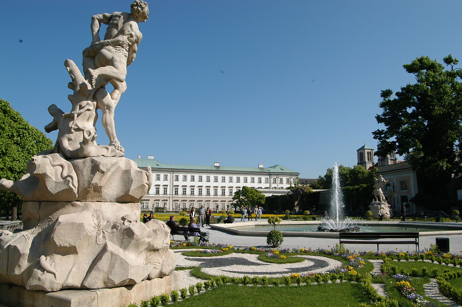 Vier-Elemente-Brunnen im Mirabellgarten Links im Vordergrund ist eines der vier Figurenpaare zu sehen, dahinter rechts im Bild der Brunnen und im Hintergrund des Fotos das Schloss Mirabell