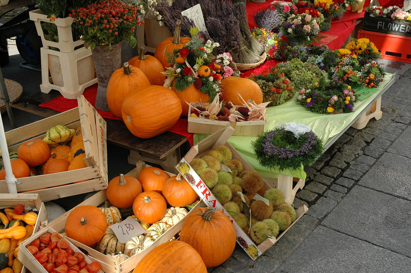 Neben Obst, Gemüse und Fleisch findet man auch Kürbis und Blumen am Markt Neue Mitte Lehen! Kisten mit unterschiedlichen Kürbissen angeordnet um einen Marktstand