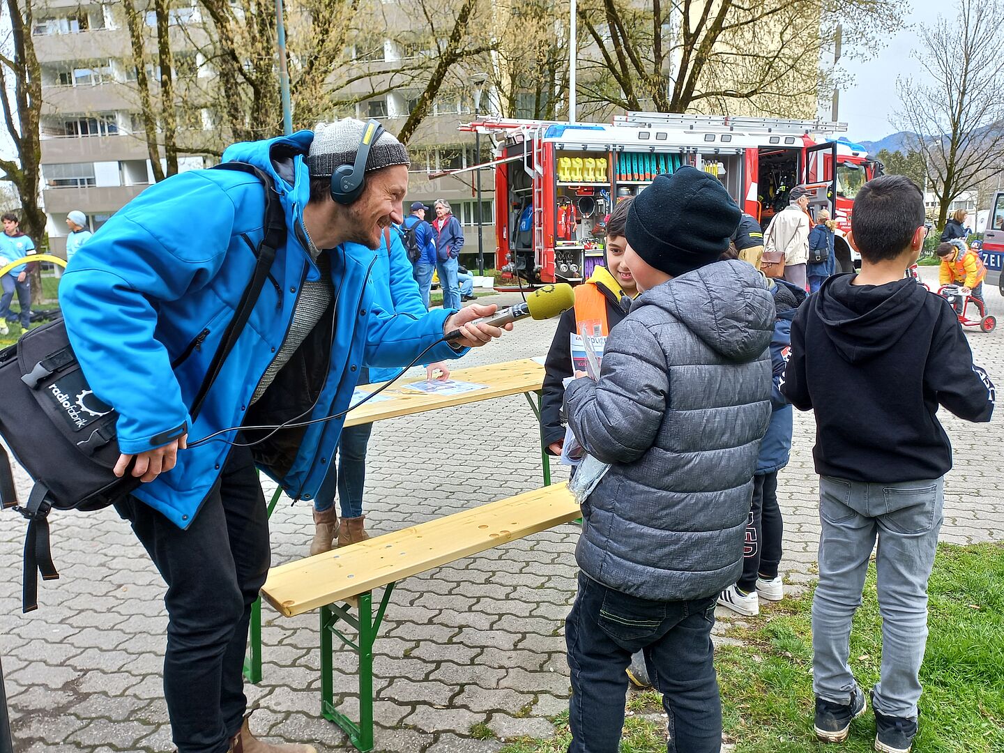 Radioreporter mit Kopfhörern und Mikrofon beim Interview mit drei jungen Burschen